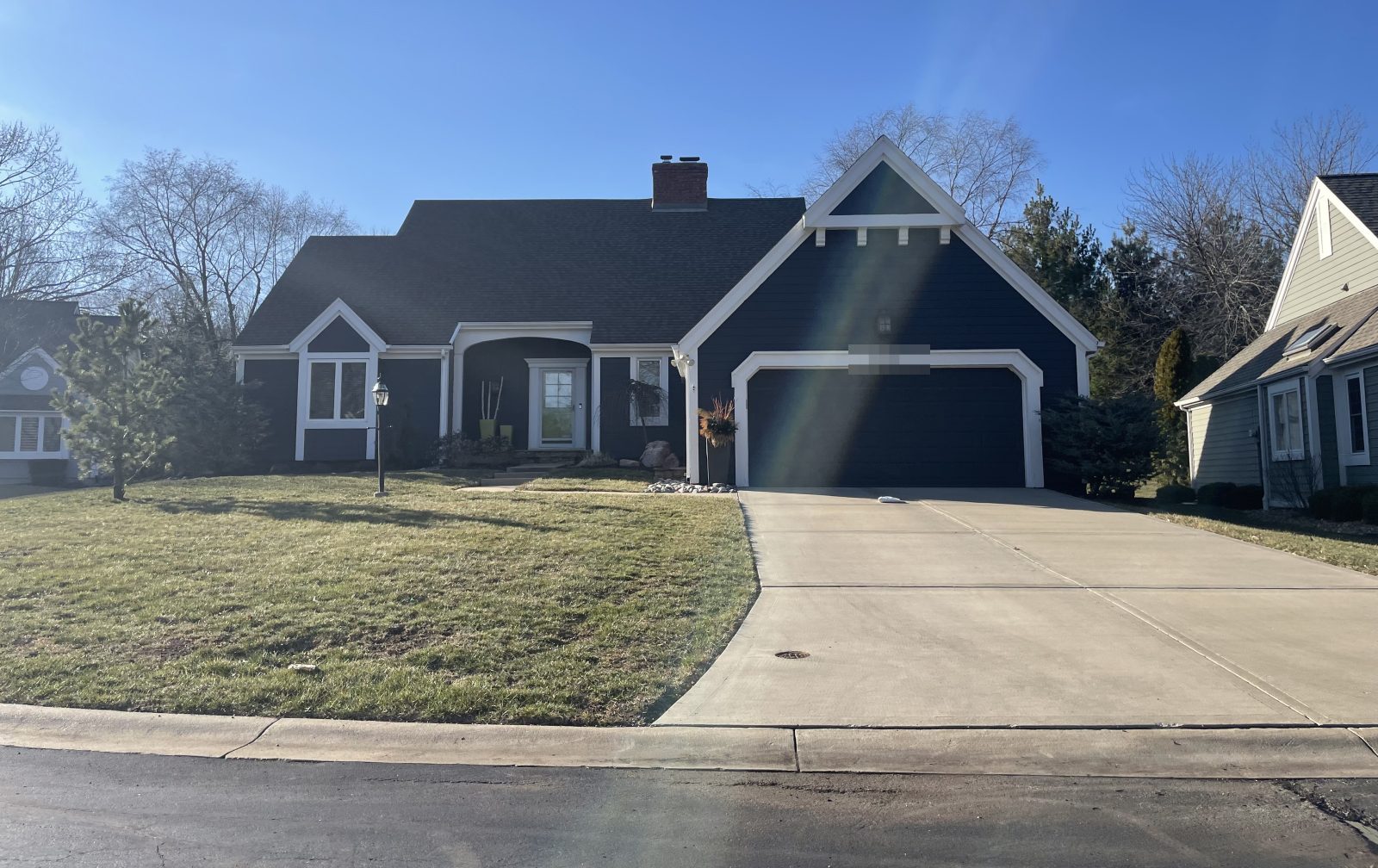 A house whose two-car garage projects toward the street under its own gable, with the front door set back to the left in the recess the projection creates, and a wide driveway running to the kerb.